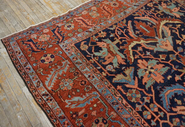 Navy and rusty red patterned rug with light blue borders rests on distressed wood planks.