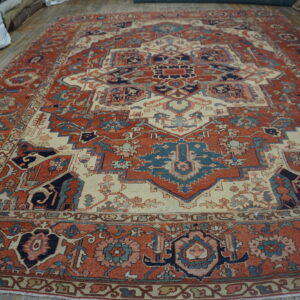 Large, intricately patterned red rug with cream, navy, and teal accents on hardwood flooring.