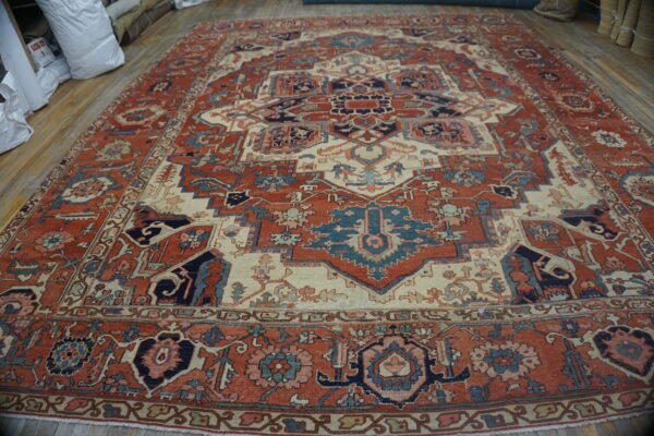Large, intricately patterned red rug with cream, navy, and teal accents on hardwood flooring.
