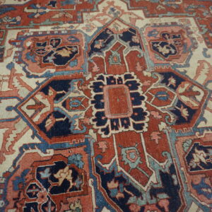 Low-pile rug with geometric and floral motifs in deep red, navy, ivory, and faded teal.