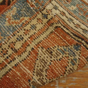 Folded rug with rust, teal, and tan geometric patterns rests on a distressed wooden floor.