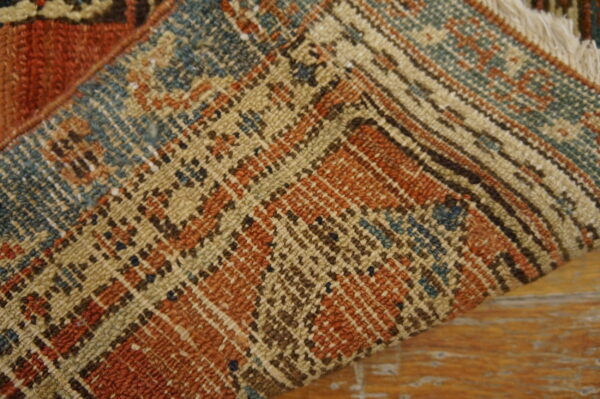 Folded rug with rust, teal, and tan geometric patterns rests on a distressed wooden floor.