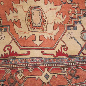 Close-up of a rug with complex geometric patterns in shades of rust, cream, navy, and light blue.