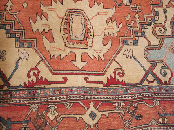 Close-up of a rug with complex geometric patterns in shades of rust, cream, navy, and light blue.