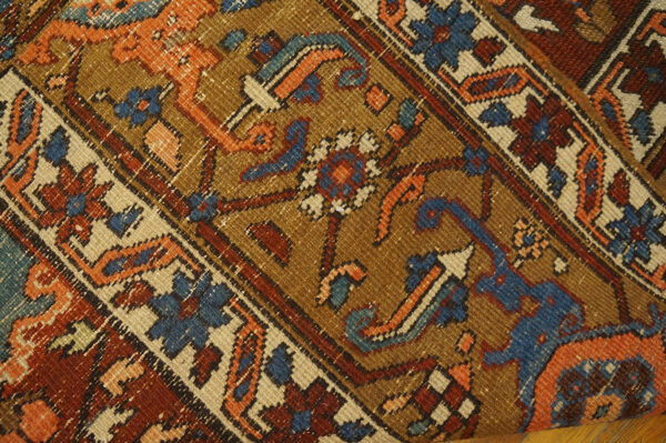 Close-up of a rug with a camel field, rust, blue, and orange geometric and floral motifs on wood flooring.