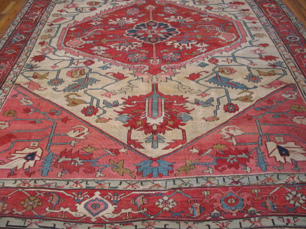 Red, cream, and blue rug featuring a bold geometric medallion and floral patterns on wood flooring.