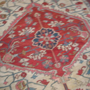 Low-pile rug with a dense red geometric medallion and scattered blue, cream, and pink botanicals.