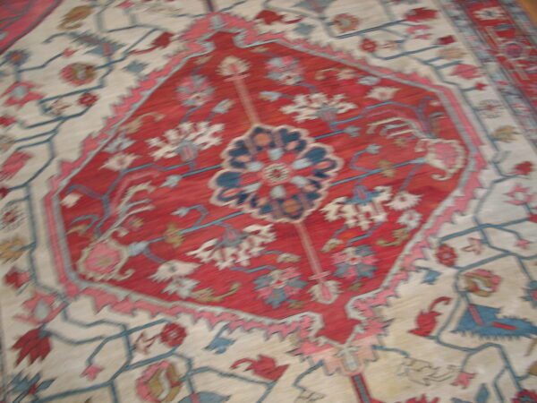 Low-pile rug with a dense red geometric medallion and scattered blue, cream, and pink botanicals.