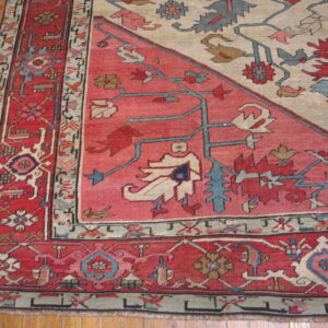 Detail of a low-pile rug showing red, cream, and blue stylized motifs bordering hardwood flooring.