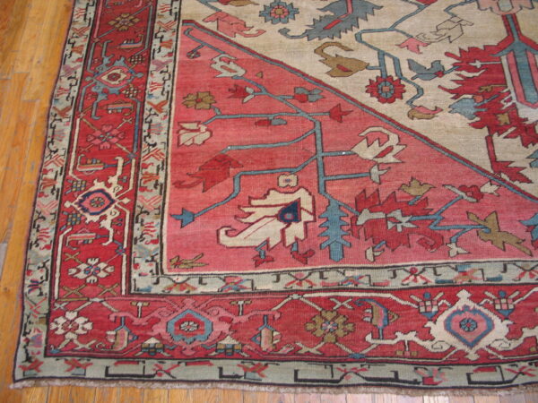 Detail of a low-pile rug showing red, cream, and blue stylized motifs bordering hardwood flooring.
