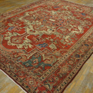 Red and ivory rug with geometric designs and blue accents covers worn wood flooring.