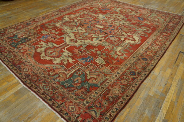 Red and ivory rug with geometric designs and blue accents covers worn wood flooring.