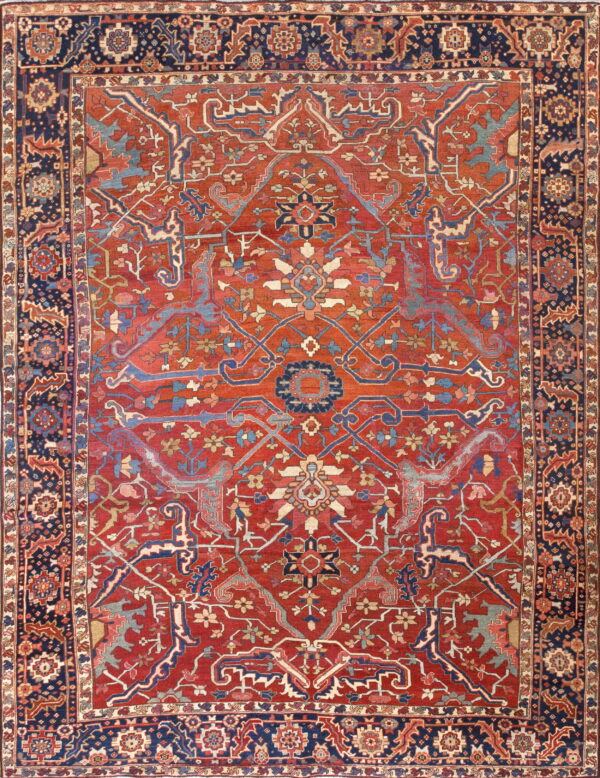 Intricate traditional rug featuring a red field, navy border, and detailed blue and tan patterns.