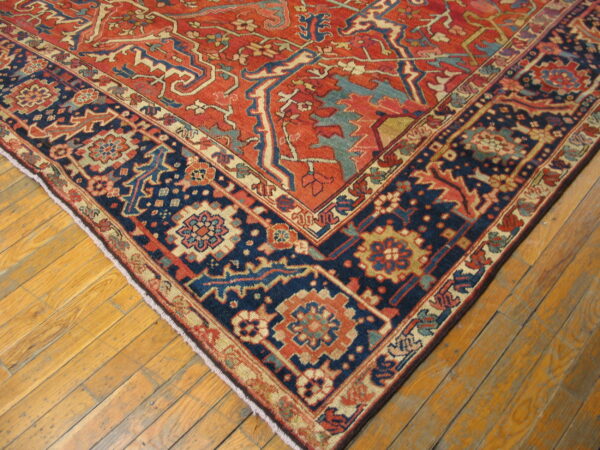 Red and indigo patterned rug with geometric designs resting on distressed wooden plank flooring.