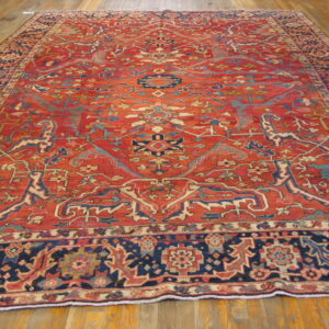 Large rug in red, navy blue, and teal with detailed floral patterns lies on hardwood flooring.