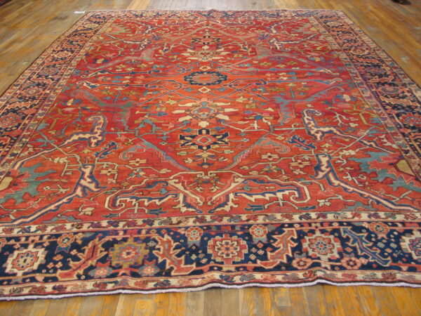 Large rug in red, navy blue, and teal with detailed floral patterns lies on hardwood flooring.