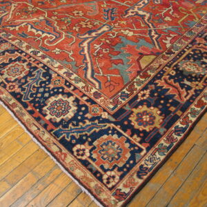 Ornate red and navy patterned rug corner with contrasting light blue and beige accents on distressed wood floor.