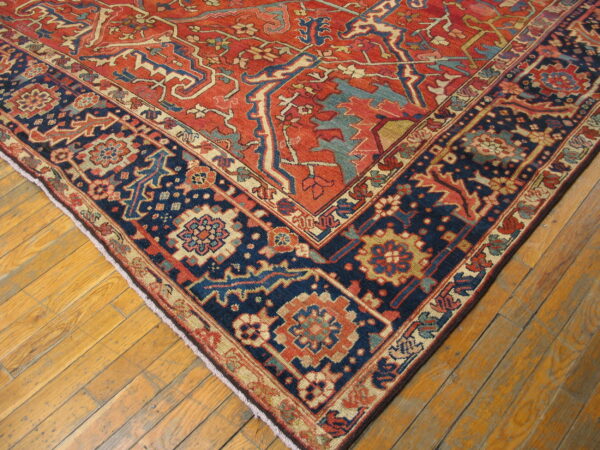 Ornate red and navy patterned rug corner with contrasting light blue and beige accents on distressed wood floor.