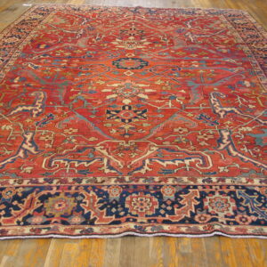 Large traditional rug with intricate red, navy, and teal patterns covering a light brown wood floor.