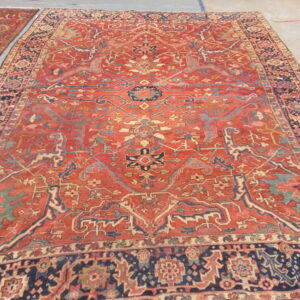 Rust and navy traditional rug with intricate motifs lying flat on a gray cloth over concrete flooring.