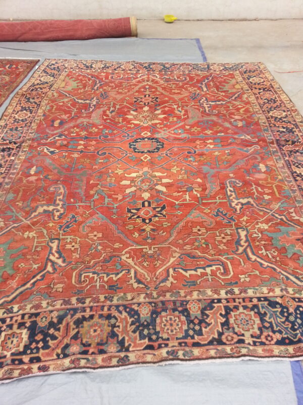 Rust and navy traditional rug with intricate motifs lying flat on a gray cloth over concrete flooring.