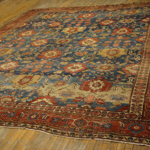 Traditional blue, rust, and gold patterned area rug rests on a heavily worn plank wood floor.