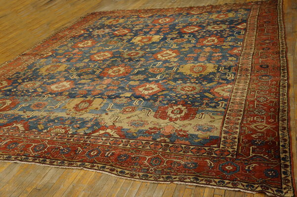 Traditional blue, rust, and gold patterned area rug rests on a heavily worn plank wood floor.