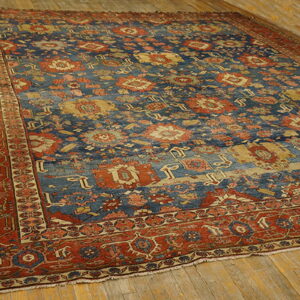 Large traditional rug with a heavily patterned blue field and rust border, placed on distressed wood plank flooring.