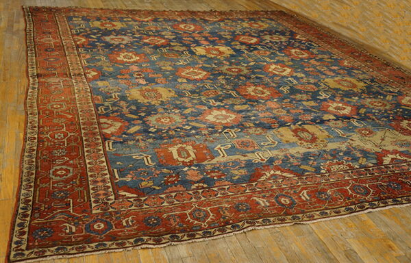Large traditional rug with a heavily patterned blue field and rust border, placed on distressed wood plank flooring.