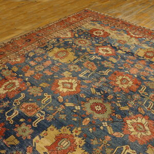 Distressed blue and red traditional rug with low pile lying on golden hardwood flooring.
