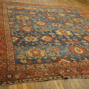 Blue and rust patterned rug with dense traditional motifs, positioned on wide plank wood flooring.