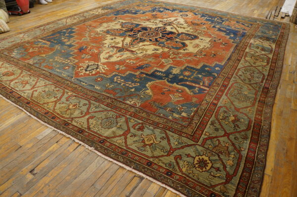 Rust, blue, and cream patterned area rug with a wide sage border sits on distressed wood floors.