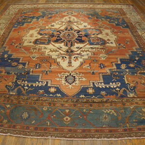 Large traditional rug featuring a geometric medallion pattern in navy, terracotta, and cream on wood flooring.