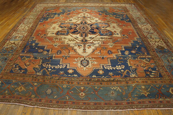 Large traditional rug featuring a geometric medallion pattern in navy, terracotta, and cream on wood flooring.