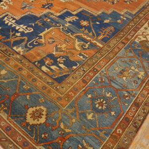 Ornate rug corner displaying rust orange, navy blue, and teal geometric patterns on a wooden floor.