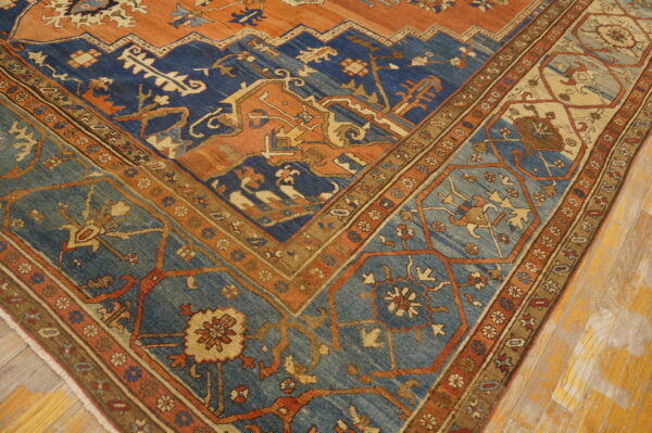 Ornate rug corner displaying rust orange, navy blue, and teal geometric patterns on a wooden floor.