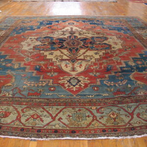 Rust red, blue, and cream traditional medallion rug displayed on polished wood flooring.