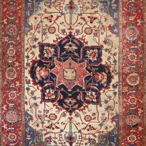A complex traditional low pile rug with a cream field, navy medallion, and wide red floral borders.