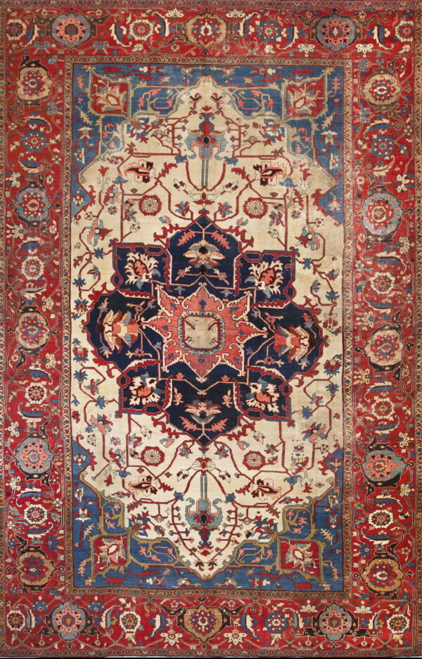 A complex traditional low pile rug with a cream field, navy medallion, and wide red floral borders.