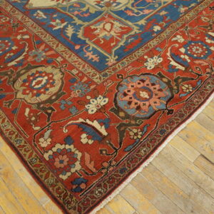 Traditional red and blue low-pile rug with complex floral patterns lying on wide plank wood flooring.