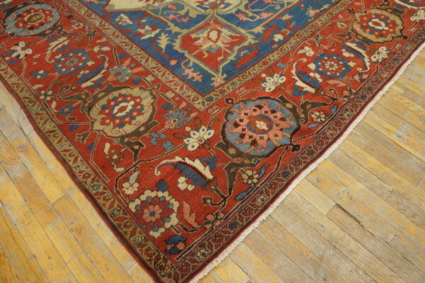 Traditional red and blue low-pile rug with complex floral patterns lying on wide plank wood flooring.