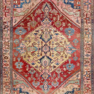 Low-pile rug with geometric patterns in red, gold, blush pink, and blue, centered by a large diamond motif.