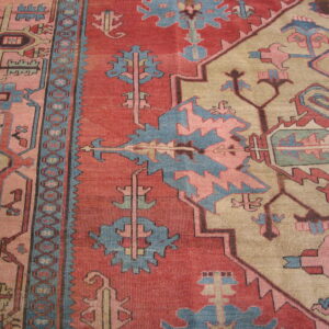 Close-up view of a tribal patterned rug in brick red, dusty blue, pink, and tan.