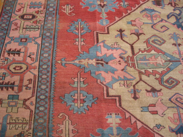 Close-up view of a tribal patterned rug in brick red, dusty blue, pink, and tan.