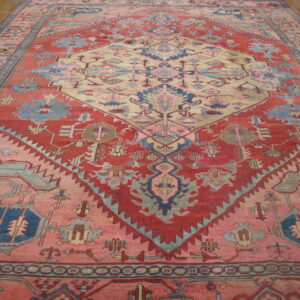 Oversize rug with a large beige geometric diamond framed by red, pink, and blue designs on wood floors.