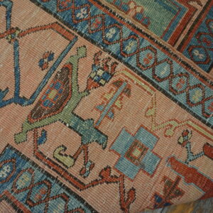 Geometric pink, blue, and rust patterned rug lying partially rolled on weathered wood flooring.