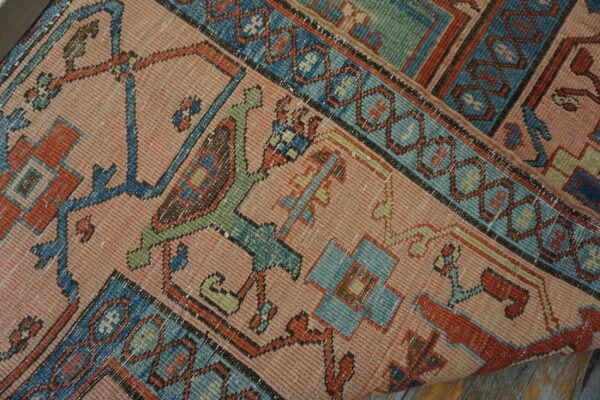 Geometric pink, blue, and rust patterned rug lying partially rolled on weathered wood flooring.