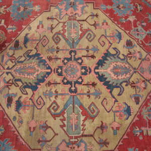 A traditional rug featuring a geometric medallion in khaki, blue, and muted pink on a reddish-maroon field.