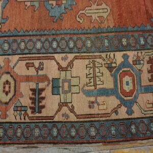 Geometric rug border in teal, rust, and light pink resting on distressed wood plank flooring.