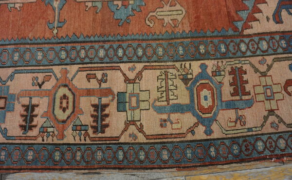 Geometric rug border in teal, rust, and light pink resting on distressed wood plank flooring.